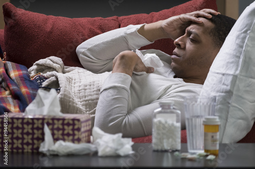Fotografie, Obraz Man sick at home on a couch with tissues and pill bottles