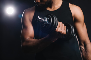 close-up partial view of muscular african american sportsman training with dumbbell on black