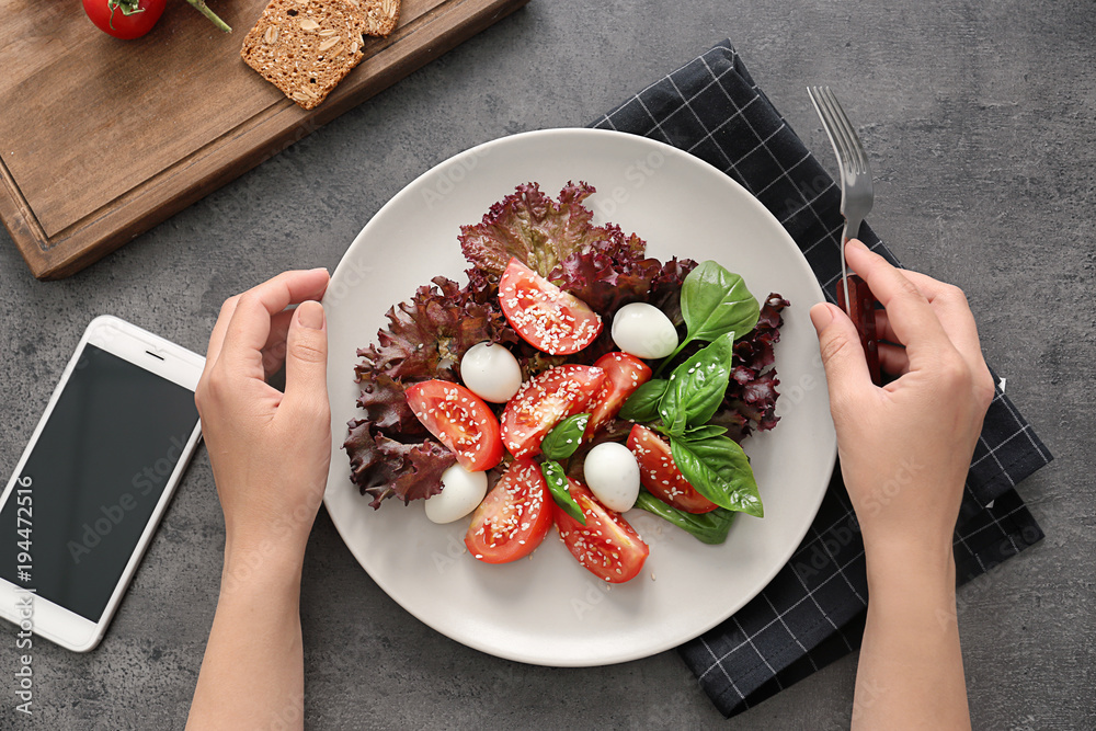 Woman's hands holding fork and plate with fresh salad on table