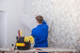 Fototapeta  - Young worker making repair in room, wallpapering on wall
