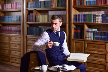Leinwandbilder - Professor with thoughtful face reads book and drink tea