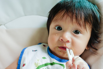 Baby cry and bite his spoon while being feeding the food on high chair. His face expressed he don't like the food