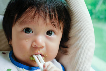 Wall Mural - Baby cry and bite his spoon while being feeding the food on high chair. His face expressed he don't like the food