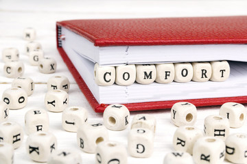 Wall Mural - Word Comfort written in wooden blocks in red notebook on white wooden table