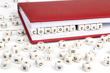 Wall Mural - Word Comfort zone written in wooden blocks in red notebook on white wooden table.