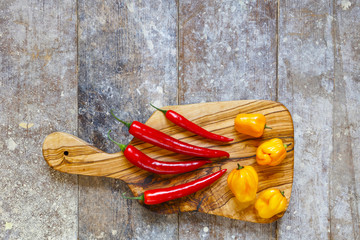 Red and yellow hot peppers on cutting board on old wooden table with copy space above