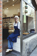 © Maskot - Portrait of smiling senior baker sitting on checkout counter in bakery