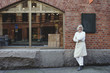 © Maskot - Full length of smiling baker standing on sidewalk against brick wall