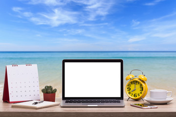 Fototapete - Modern laptop computer, Coffee cup, alarm clock, notebook and calendar on wooden table and view of tropical beach. Saved with clipping path. Work and holiday concept