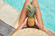 © WHstudio Leushin N - Unrecognizable slim young woman keeps juicy pineapple in hands, spends free time near swimming pool with blue water, has exotic summer diet. Relaxation and eating concept. Season for good rest