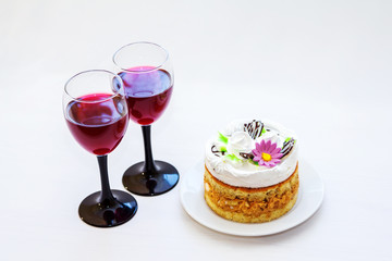 Two elegant glasses of red wine and biscuit cake on a white plate. Festive drinks and dessert for celebration on white background.