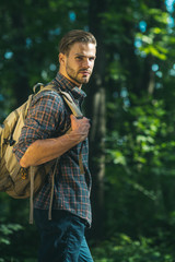 Travel, tourism, adventure, hike and people concept - bearded man with backpack hiking in forest and breathes pure air on sunny day.