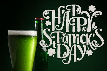 Wall Mural - close up view of bottle and glass of beer with happy st patricks day lettering on green background