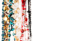 An Abstract Closeup Of Colourful Beaded Necklaces Hanging In A Row Against A White Background, With Negative White Space To The Right Of The Necklaces