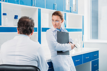 Wall Mural - partial view of female scientist with notepad in hands standing near colleague in lab