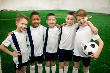 Happy football team of five successful members in uniform looking at camera on pitch