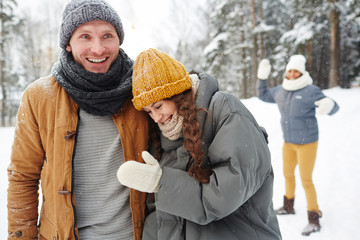 Wall Mural - Laughing young couple in winterwear enjoying time with friends in winter park