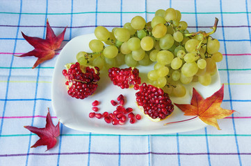 Red pomegranates and green grapes on white plate