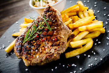 Wall Mural - Grilled steak with french fries and vegetables served on black stone on wooden table 