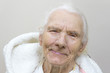Portret u uśmiechniętej siwej bardzo starej kobiety w szlafroku z kapturem.