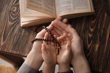 religious christian girl with her mother holding rosary beads at table, closeup