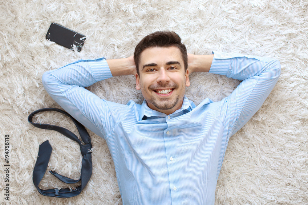 Young man with phone and tie lying on carpet, top view
