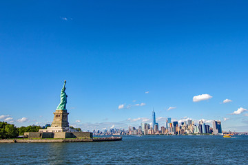 statue of liberty in foreground with unmistakeable new york’s manhattan cityscape in background view