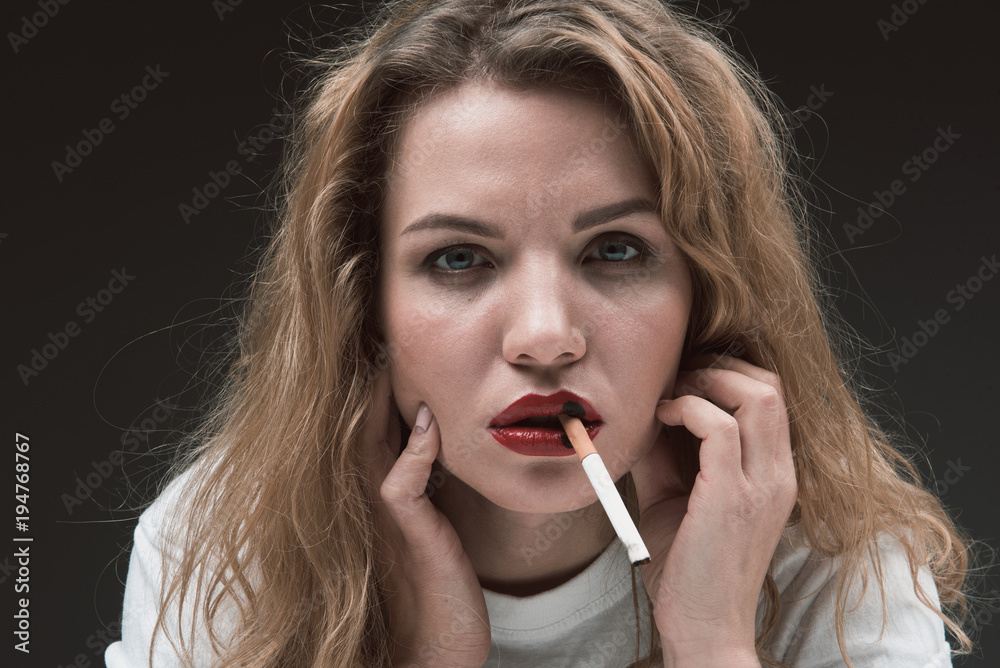 Portrait of beautiful woman holding cigarette in her mouth and looking at  camera. Isolated on background Stock Photo