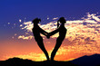 The silhouette of two young girls practicing yoga with sky background