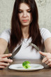 © Aliaksandr Marko - sad young brunette woman dealing with anorexia nervosa or bulimia having small green vegetable on plate. Dieting problems, eating disorder.