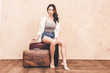 © Art_Photo - Beautiful traveler woman sit on vintage brown traveling luggage suitcase with wall background
