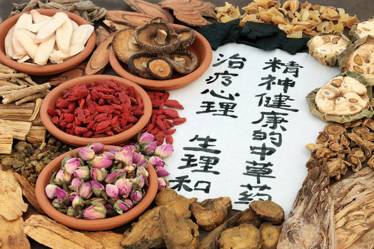 Chinese herbs used in alternative herbal medicine with calligraphy script on rice paper. Translation reads as traditional ancient chinese medicine to heal mind, body and spirit.