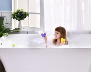 Wall Mural -  Happy little baby girl sitting in bath tub playing with duck toys  in the bathroom