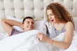 Shocked female looks under white blanket, being surprised with size of boyfriend`s genitails or sees man`s erection. Satisfied couple have good relationships. Intimate and lifestyle concept.