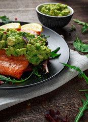 Wall Mural - Oven cooked salmon steak, fillet with avocado salsa and green on black plate. wooden table. healthy food