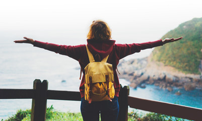 tourist traveler with backpack standing with raised hands, hiker looking to a valley in trip in spain, hipster enjoying peak of mountain background seascape ocean horizon, relax holiday concept