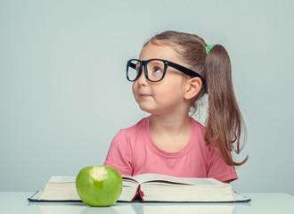 Wall Mural - beautiful cute little girl next to thick book and green apple