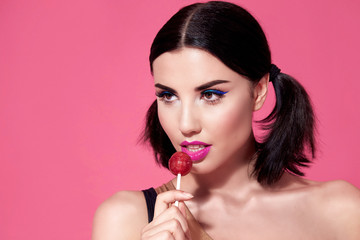 Wall Mural - Close portrait of sexy beautiful woman brunette hair style perfect bright makeup mascara pink lipstick background face care cosmetic accessory jewelry sweets lollipop diet beauty salon white teeth.