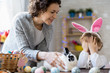 © Seventyfour - Portrait of happy young family celebrating Easter at home, mother and giving pet bunny to cute little boy with eyes closed