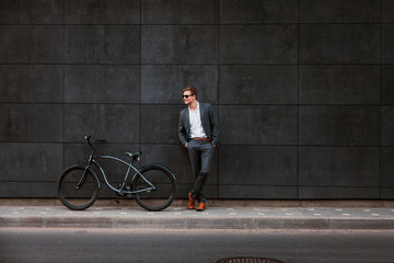 Wall Mural - Stylish young businessman in sunglasses stands near a bicycle