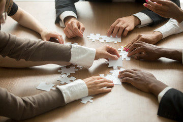 Wall Mural - Diverse business people helping in assembling puzzle, cooperation in decision making, team support in solving problems and corporate group teamwork concept, close up view of hands connecting pieces