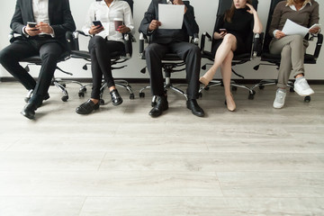 Wall Mural - Diverse business people waiting in queue holding smartphones and resumes, multiracial men and women sitting in row anticipating job interview, human resources, employment hiring concept, copy space