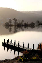 Beautiful Wooden Jetty On Lake Windemere At Sunrise With Small Island Of Trees And Misty Hills In The Background