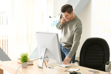 Wall Mural - Young man talking on mobile phone while working in office