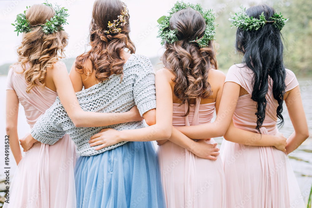three bridesmaids in powdery dresses transformers and wreaths on the head embrace the bride in a blue dress - obrazy, fototapety, plakaty 