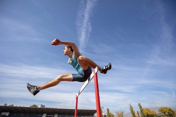 Low angle view of determined male athlete jumping over a hurdles