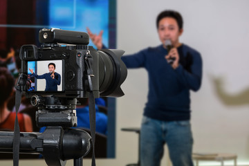 Professional digital Mirrorless camera with microphone on the tripod recording video blog of asian Speaker on the stage seminar, Camera for photographer or Video and Technology Live Streaming concept