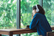 © weedezign - Happy asian casual woman listening music with headphones near window at cafe restaurant,Digital age lifestyle,chill out life.