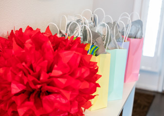 Pastel colored party gift bags with a large red decoration set up on a small table.