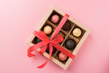 A set of assorted chocolates in a paper box with a satin pink ribbon on a pastel background.Flat layout.